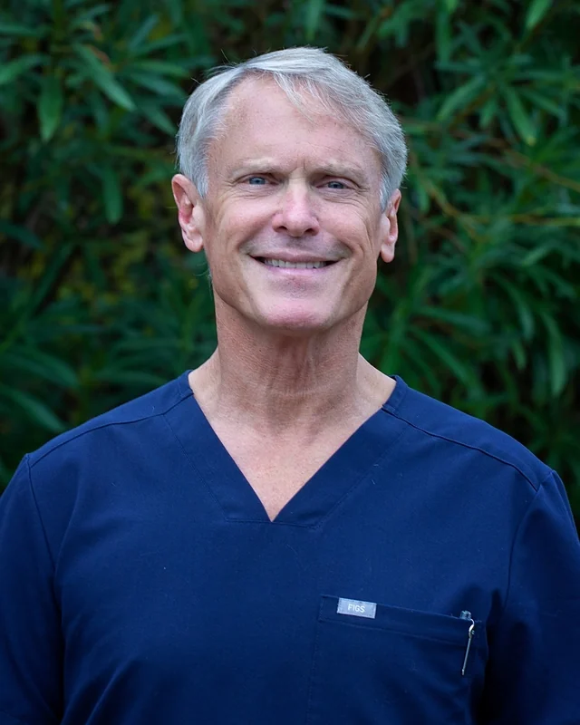 Dr. Gary Caskey, DDS, smiling, in navy scrubs.