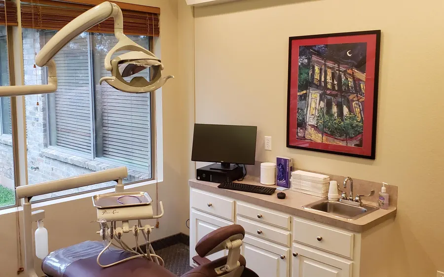 A treatment room with a window, a dental chair and a framed painting.
